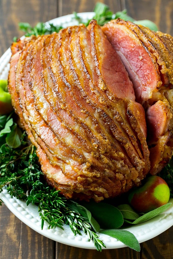 Honey Baked Ham Recipe | Glazed Ham | Holiday Ham #ham #dinner #dinneratthezoo #christmas #thanksgiving #easter A spiral cut honey baked ham on a serving platter garnished with fresh herbs.